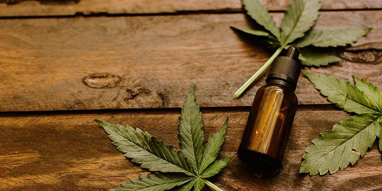 A covered brown bottle of CBD lying close to a cannabis leaf