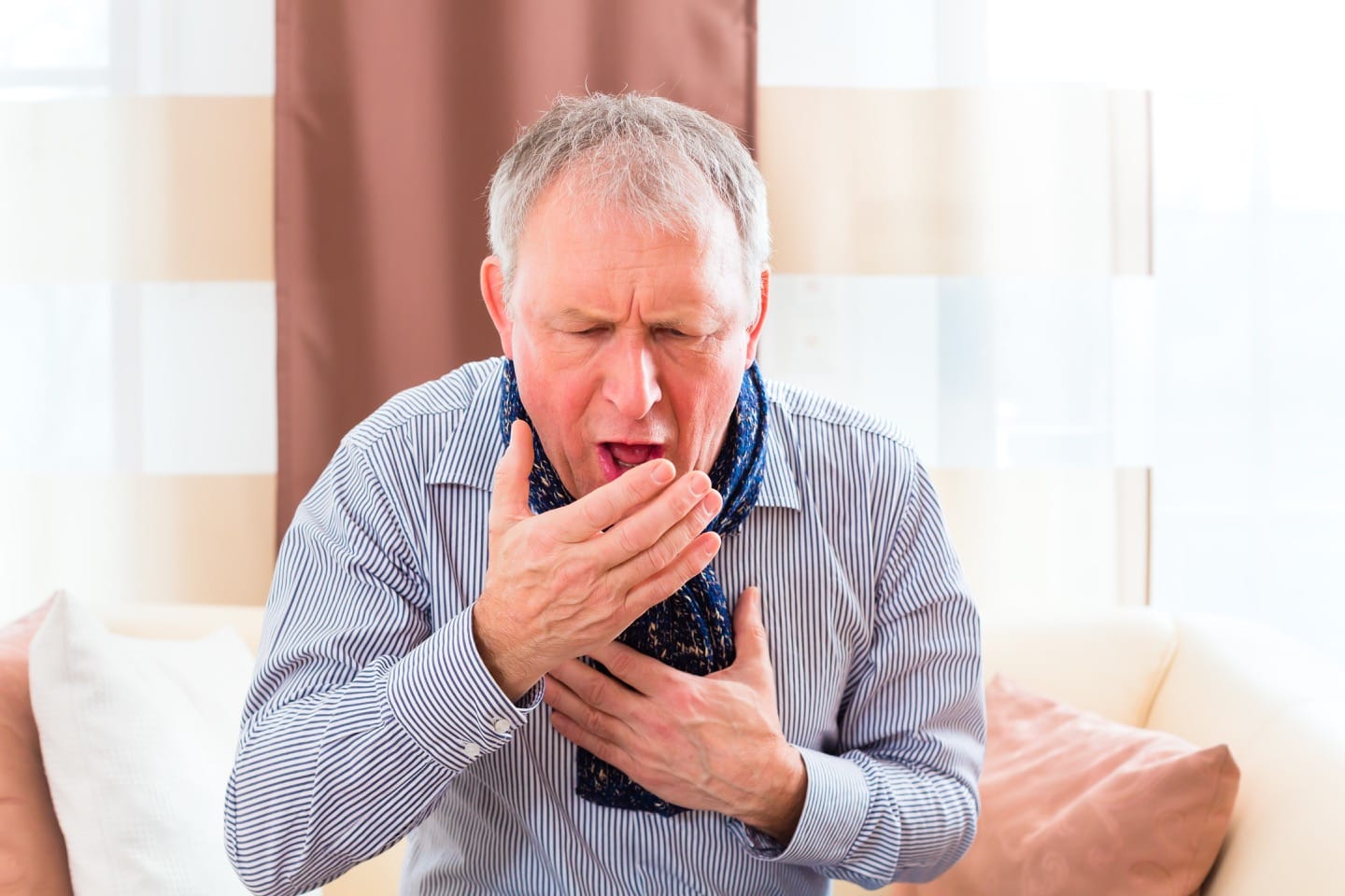 An old man coughing with one of his hand closing his mouth and the other hand to his chest