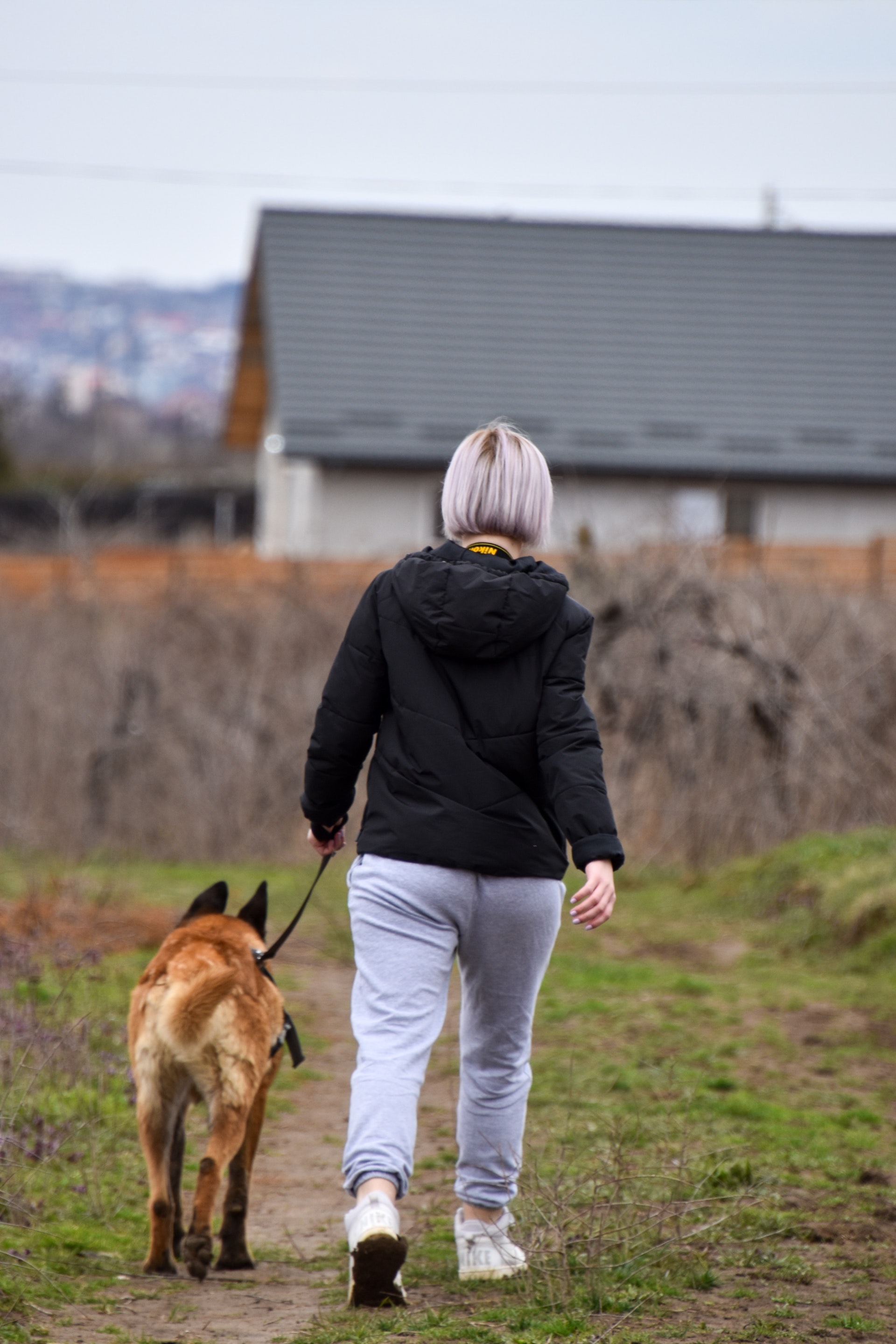 A short-haired woman in the black shirt is holding a brown dog and walking