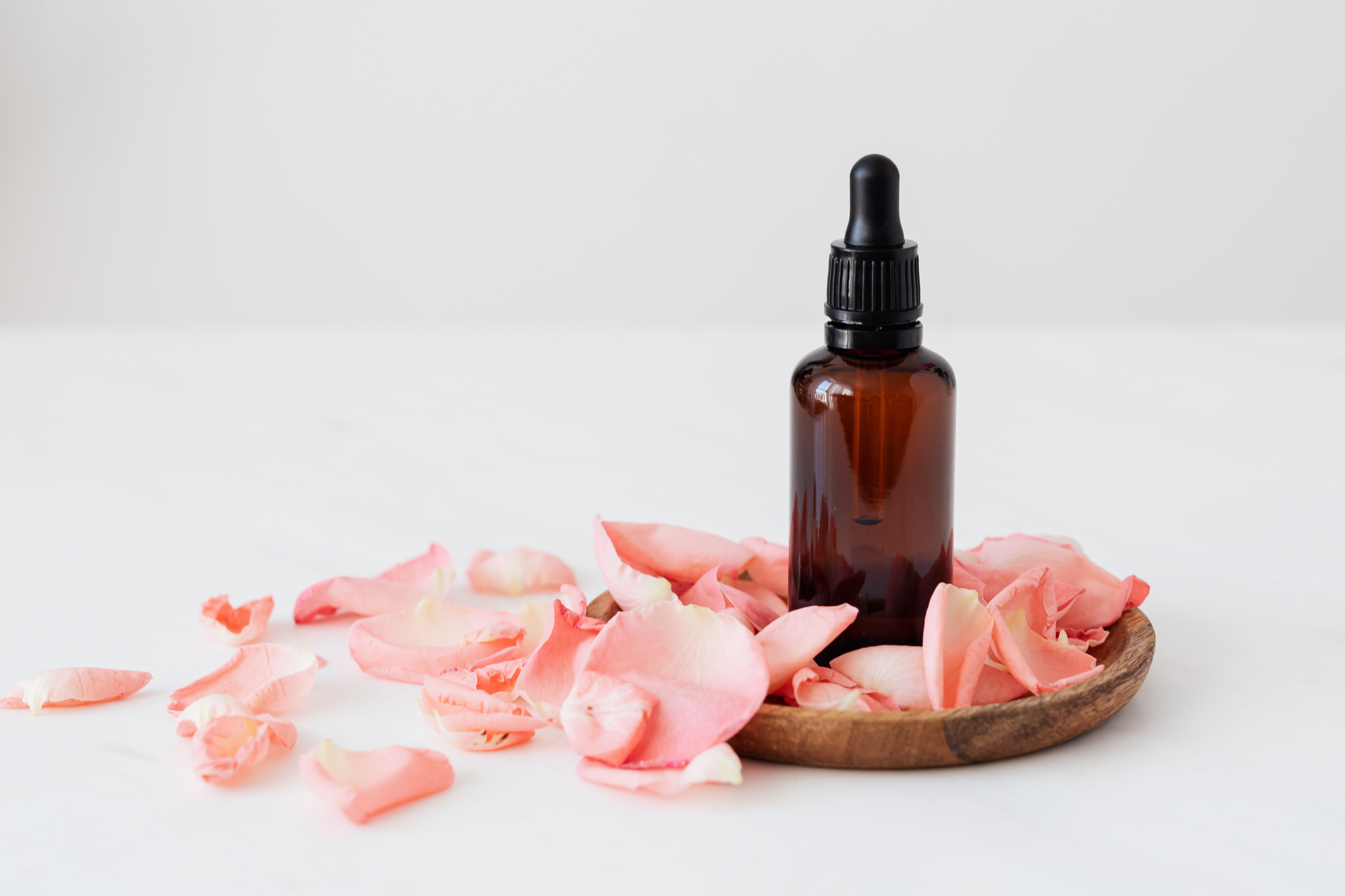 A closed brown CBD tincture bottle sitting on a wooden platter surrounded by pink flower petals