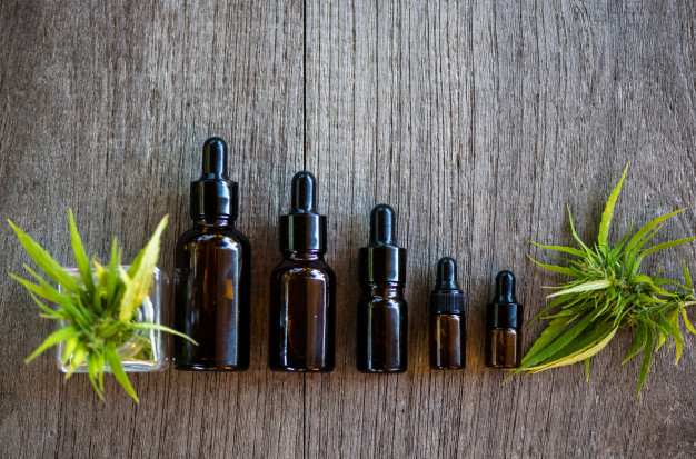 Five covered black tincture bottles arranged from the biggest to the smallest with cannabis leaves at both sides
