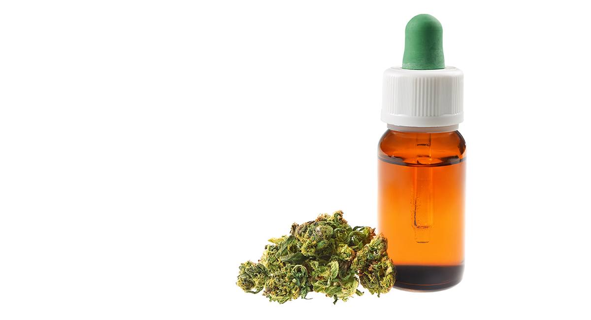 A closed brown tincture bottle with a white cover filled with CBD oil sitting beside a cannabis leaf