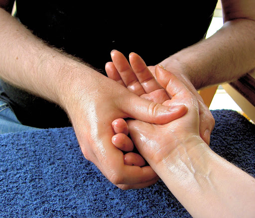 Two hands of a white man wearing a black polo massaging a white hand resting on a blue towel