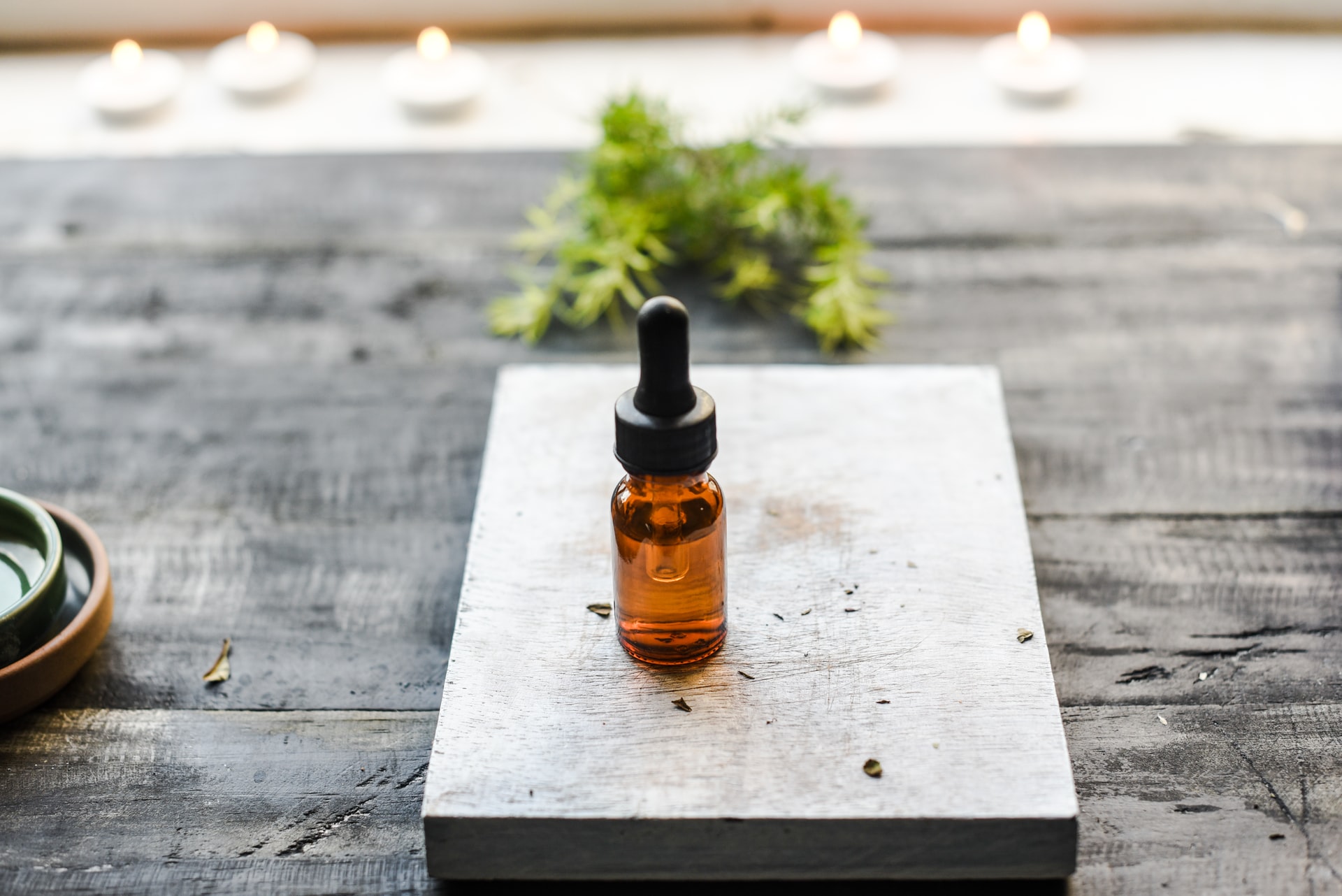 A closed bottle of CBD oil tincture sitting on a pedestal with a blurry background of a cannabis leaf
