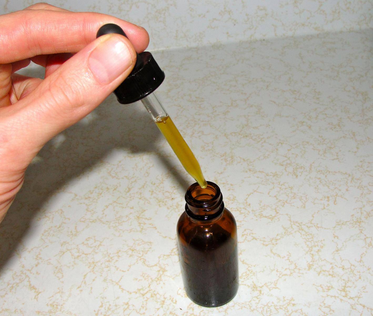 A hand bringing out a dropper filled with CBD oil from a bottle