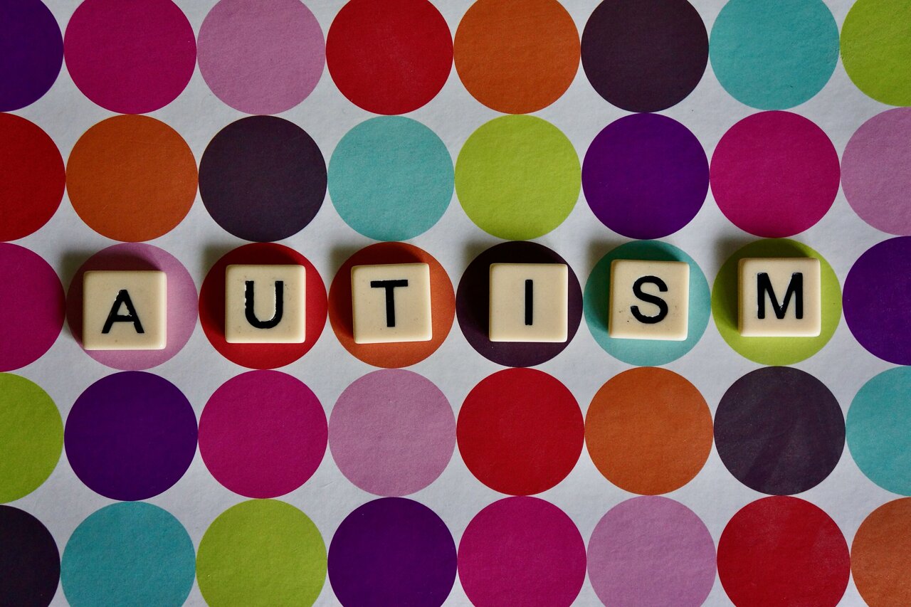 Brick letters of the word AUTISM spelt horizontally on a background of many circles in different colors
