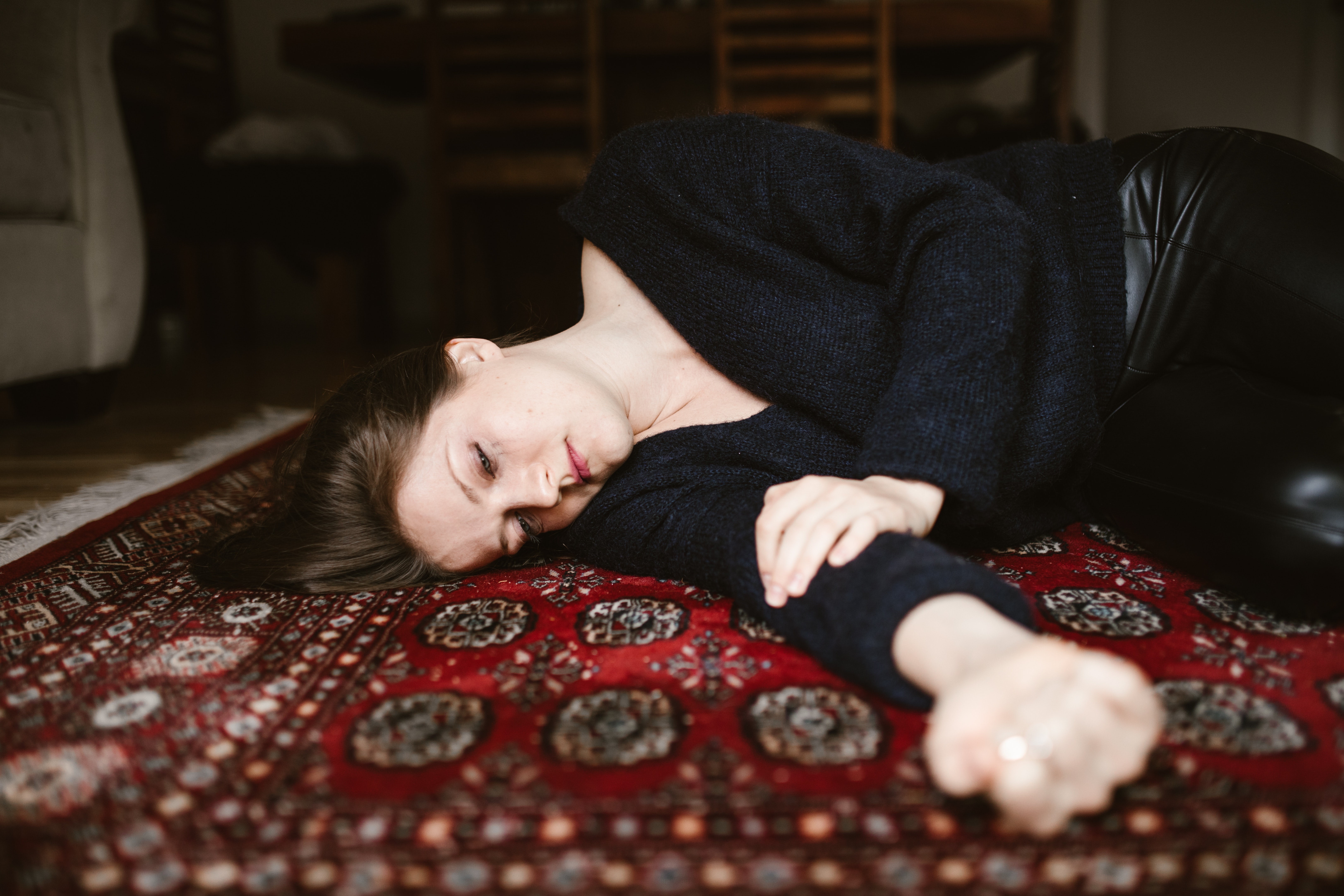 A Caucasian woman a blue t-shirt and a black pant laying on a carpet with her eyes half closed