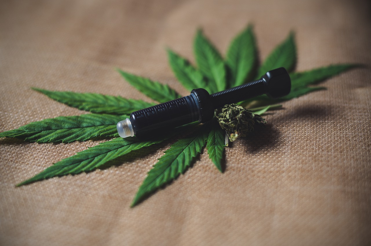 A black vape pen sitting on a cannabis leaf