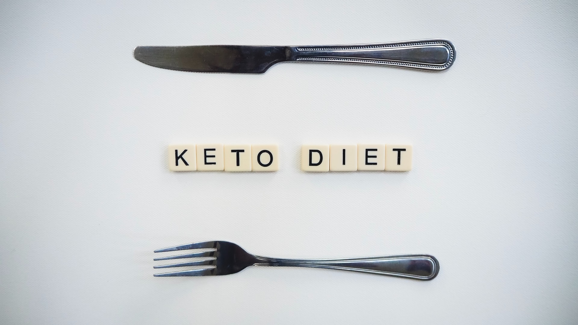 The word Keto Diet written on some scrabble tiles with a spoon and fork laying on both sides of the tiles