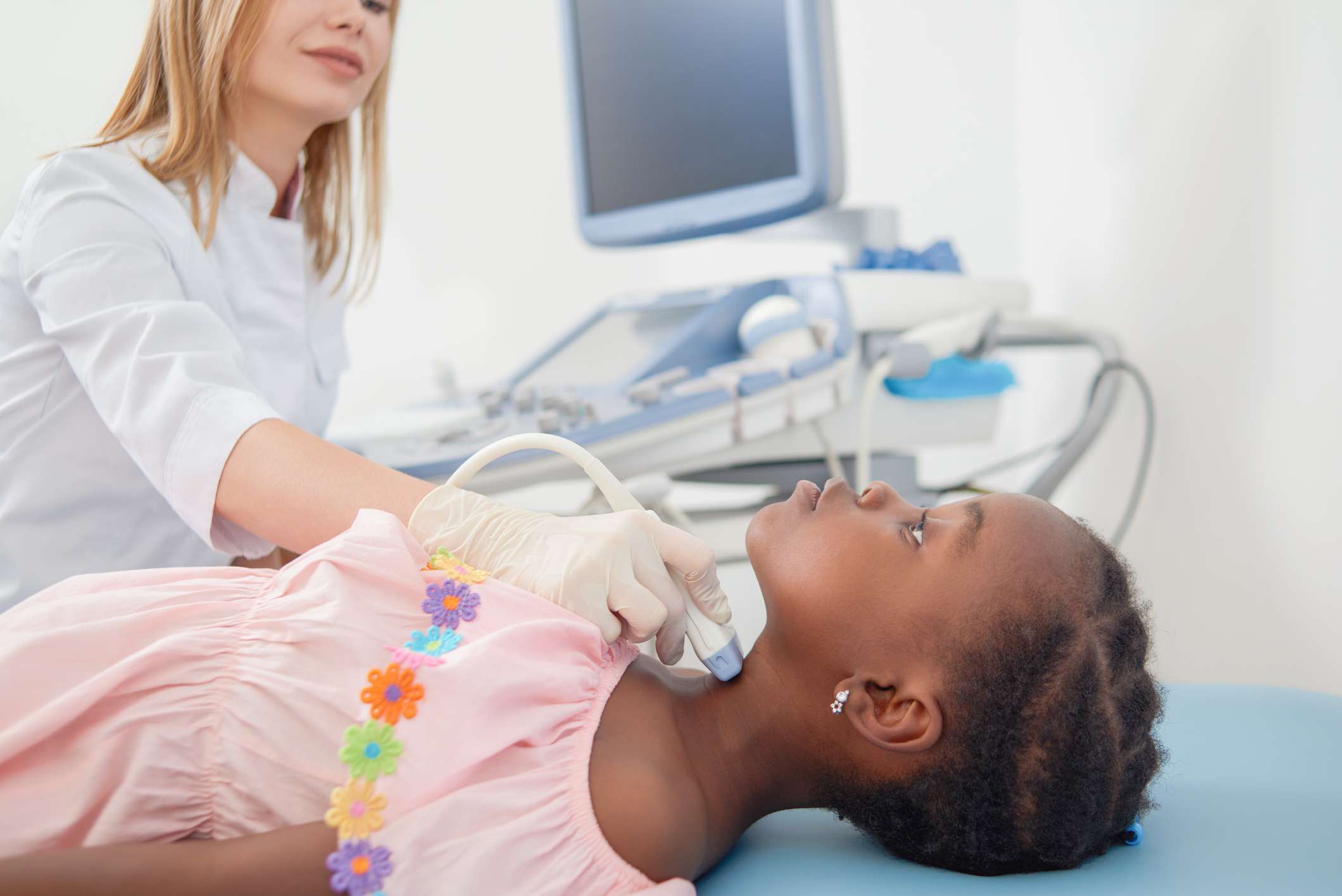 A Caucasian female doctor doing an ultrasound on the neck of a black female child