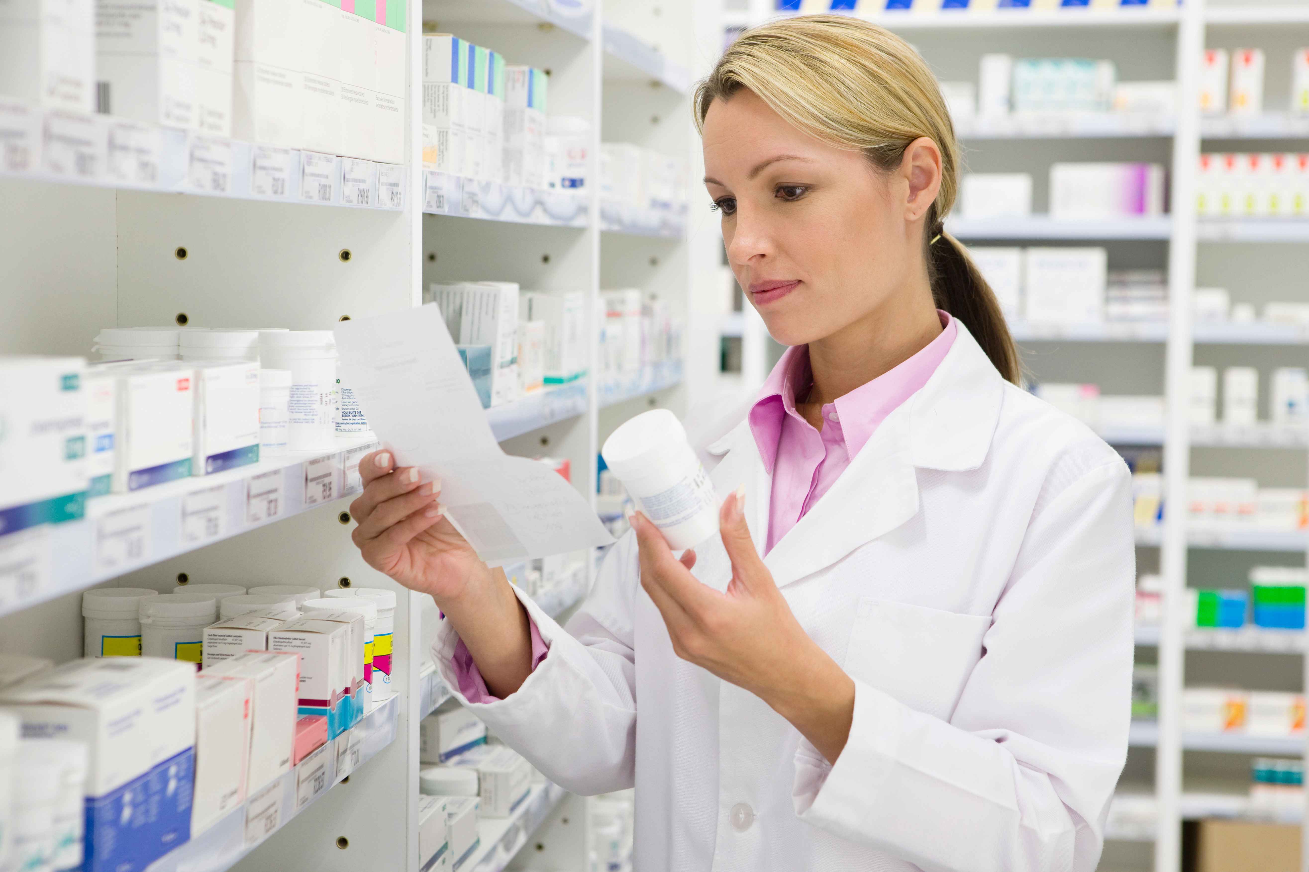A woman doctor is holding a paper and white plastic bottle in her hands while standing in a pharmaceutical store.