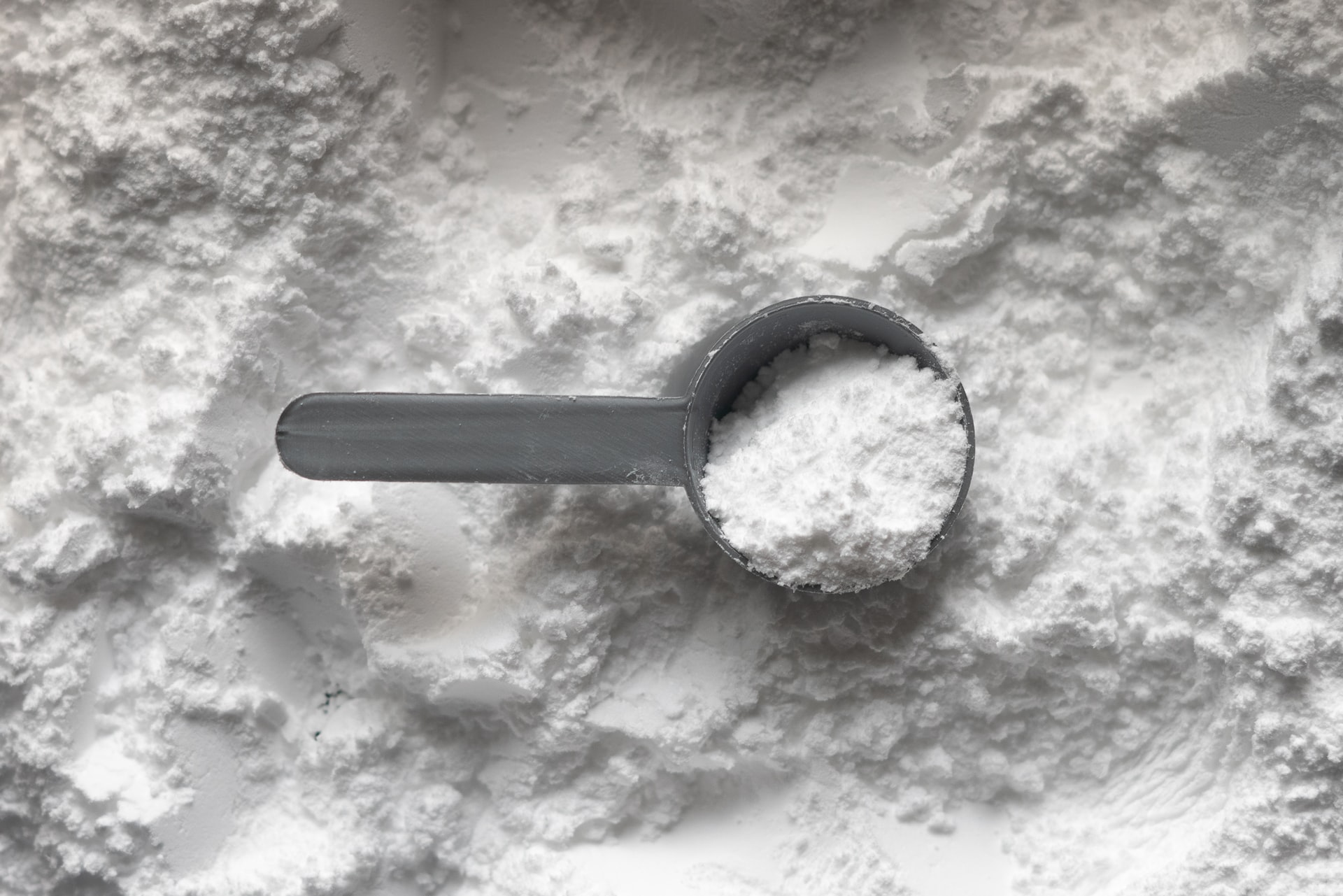 A plastic spoon filled with lactate powder sitting on a platform full of lactate powder
