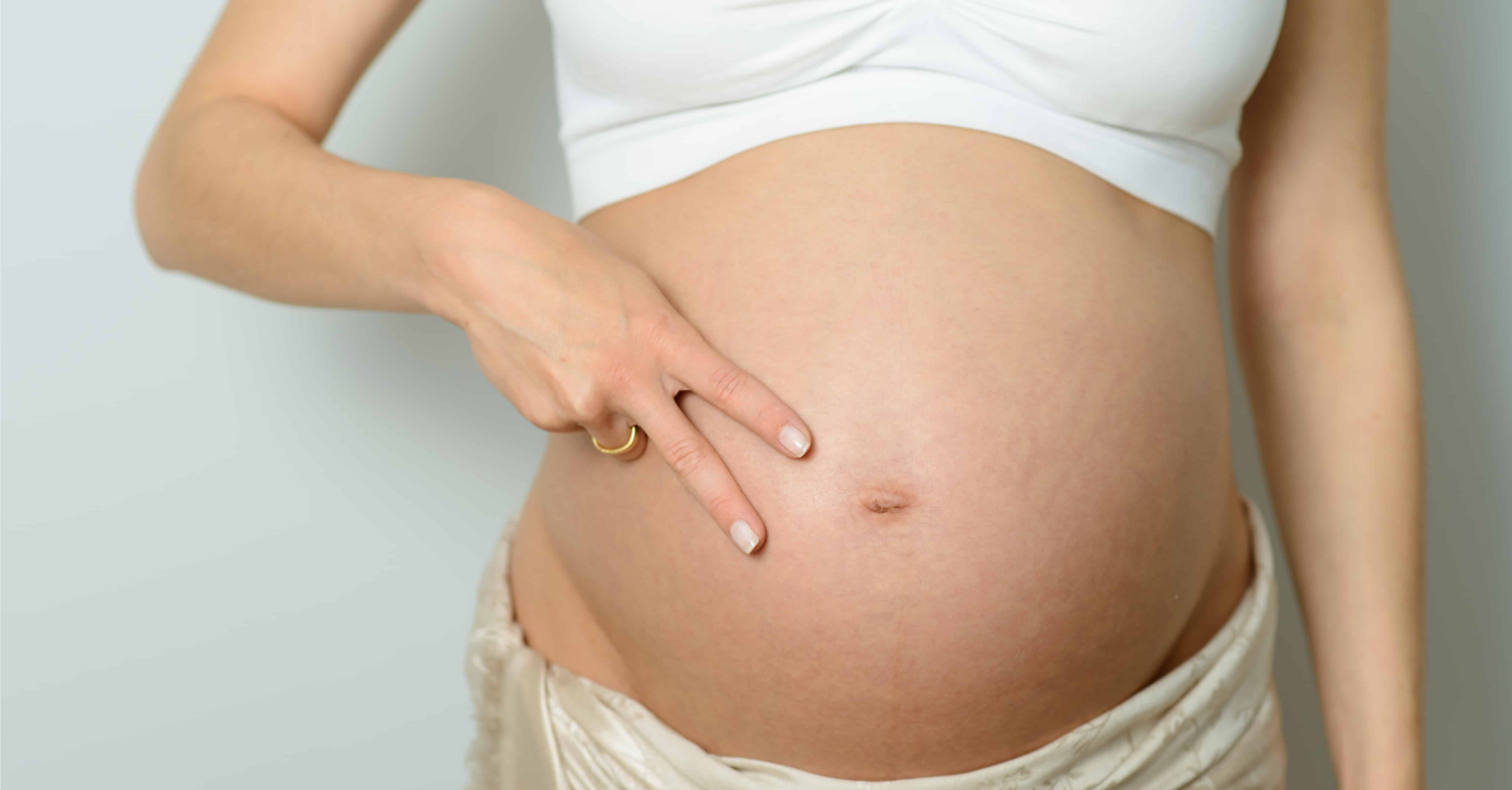 A pregnant woman showing a sign of two with her fingers on her stomach
