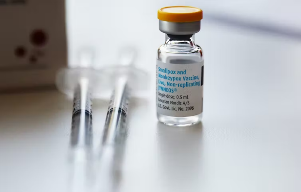 A covered bottle of the JYNNEOS smallpox and monkeypox vaccine beside two syringes