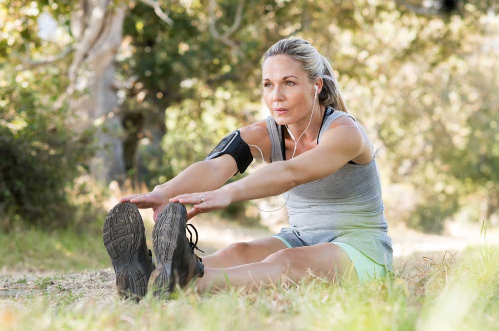 A woman wearing an exercise attire sitting on a grass while doing an exercise routine