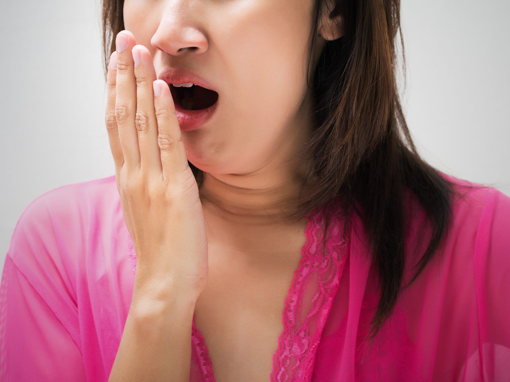 A woman wearing a pink cloth blowing her breath into her hand while smelling it