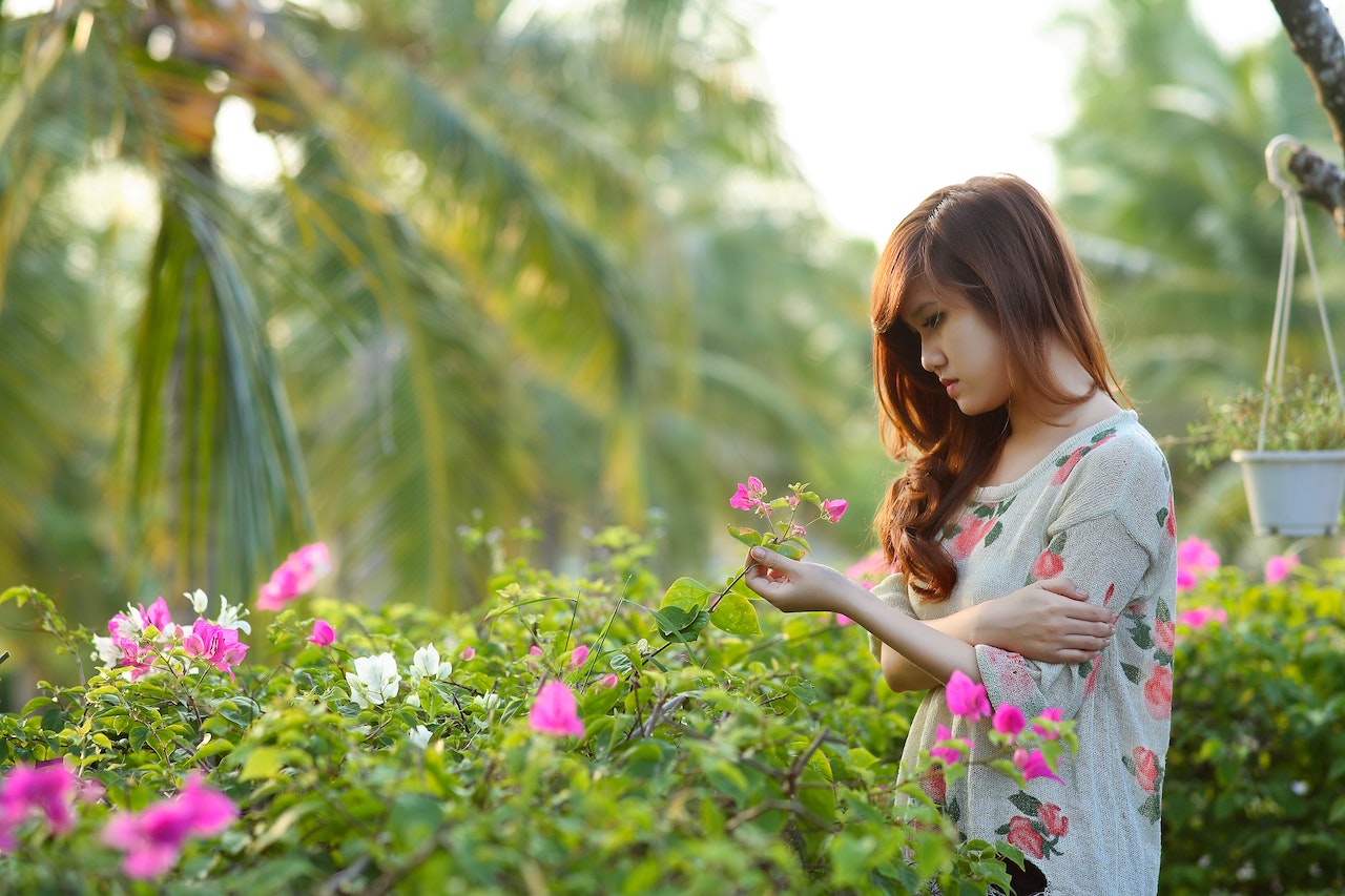 Girl Wearing White, Pink, and Green Floral Dress Holding Pink Bougainvillea Flowers