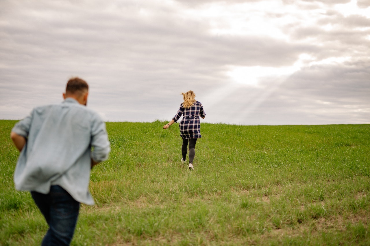 Man and Woman Running Through a Green Field 