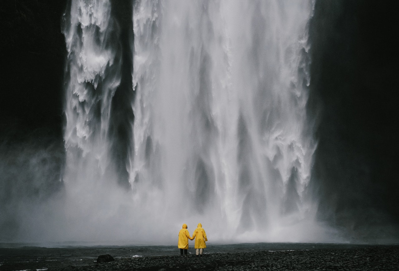 Anonymous travelers holding hands against spectacular waterfall